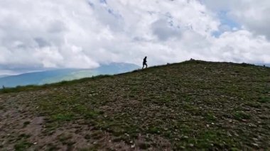 Erkek sporcu yaz mevsiminde dağlarda bir dağ manzarasının arka planında koşuyor. Hava görünümü spor içeriği