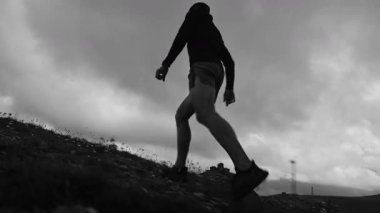 Siyah beyaz monokrom video. Yüksek kontrastlı. Genç sporcu dağ manzarası ve bulutların zeminine karşı yüksek dağlara tırmanıyor..