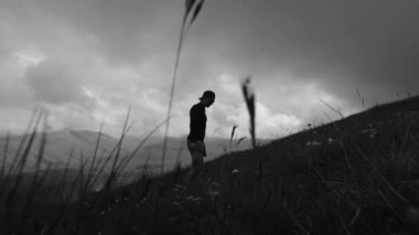 Siyah beyaz monokrom video. Yüksek kontrastlı. Genç sporcu dağ manzarası ve bulutların zeminine karşı yüksek dağlara tırmanıyor..