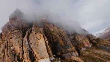 İHA saldırısı, panoramik manzaranın üstünde yüksek dik kayalık dağlar, parçalı bulutlu gökyüzü, Alplerde yürüyüş, görkemli manzara, sinematik uçuş.