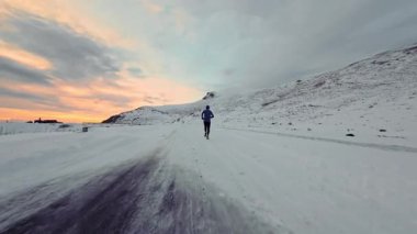 Arka planda karlı dağlarla birlikte koşan genç bir adamın hava aracı görüntüsü. Sağlıklı koşu ve egzersiz konsepti, yüksek hızlı insansız hava aracı FVP atışı, yavaş çekim.