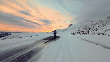 Genç sporcu kış dağlarında gün batımında dışarıda koşuyor. Spor giyimli bir adam aktif bir hayat sürüyor..
