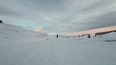 Genç beyaz erkek atlet Pashmina 'da yürüyor ve kış mevsiminde, dağlarda, gün batımında karla ve dağlarla çevrili sıcak giysiler içinde. Alacakaranlıkta koşuyor. Fpv spor insansız hava aracından hava görüntüsü.
