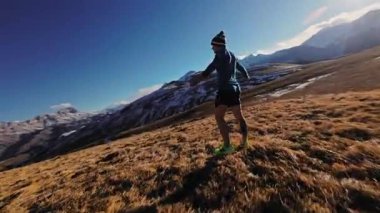 Atletik koşucu, sonbaharda karlı zirvelere karşı dağda koştuktan sonra dinleniyor. İnsansız hava aracı etrafında uçuyor..