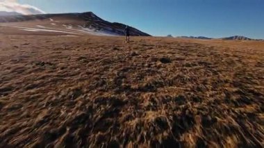 Sonbahar ya da kış aylarında dağ vadisinde arka planda dağlarla koşan spor giyimli FPV insansız hava aracı. Profesyonel koşucunun spor insansız hava aracı görünümü.