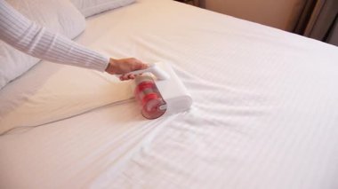 Beyaz kadın yatak akarlarından çarşaf temizliyor. Toz çarpma fonksiyonu ve ultraviyole dezenfeksiyonu olan bir yatak süpürgesi kullanıyor.