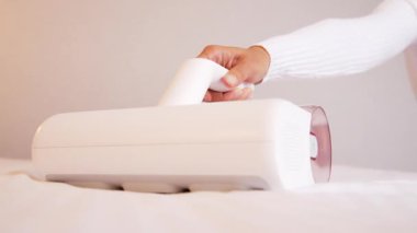 Elektrik süpürgesi ultraviyole lambalı ve tozlu karıncalardan döşekleri temizlemek için. Bir kadının eli yatak odasındaki yatağı temizleyip dezenfekte ediyor..