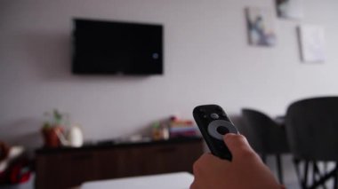Televizyonun uzaktan kumandasını tutan ve televizyon kanallarını değiştiren bir kadının yakın çekimi. Elin arka planında odağı bozuk bir televizyonu olan bir duvar var. Bulanık TV.