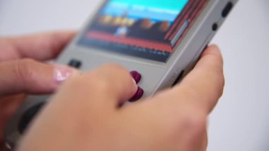 Yüzeyin derinliğine yakın çekim. Genç beyaz bir kadının ellerinde tanımlanamayan portatif retro konsol. Kız, eski konsol oyunlarına benzemek için retro oyunlar oynuyor.