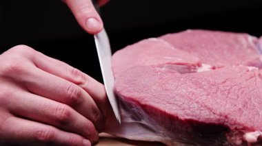 Bir kasap, karanlık bir odada büyük bir bıçakla fasyayı biftekten ayırır..