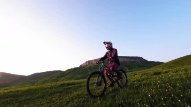 Yakın plan genç erkek binici, dağlarda yavaş çekimde bisikletiyle bisiklete biniyor. Fpv insansız hava aracının epik kaya dağları görüntüsü.