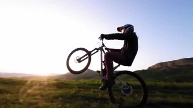 Motosikletlinin arazi yolundaki dağ bisikletinde manuel arka tekerlek numarası yaparken çekilmiş hava takibi fpv görüntüsü. Erkek bisikletçinin dağlarda aşırı doğa sporu yapması. Gün batımında yavaş çekim