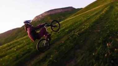 Miğferli ve maskeli genç bir sporcu gün batımında arka tekerlere binip pedal çeviriyor. Fpv insansız hava aracında hava görüntüsü