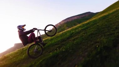 Motosikletlinin arazi yolundaki dağ bisikletinde manuel arka tekerlek numarası yaparken çekilmiş hava takibi fpv görüntüsü. Erkek bisikletçinin dağlarda aşırı doğa sporu yapması. Gün batımında yavaş çekim