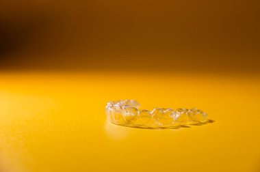 Renkli sarı arka planda, yakın plan, yan görünüşte şeffaf diş hizalayıcıları. Dişleri düzeltmek için modern yöntemler.