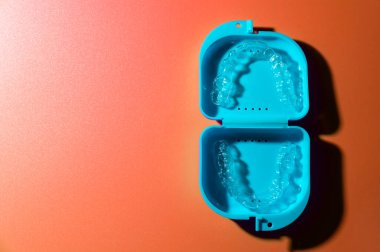 Şeftali arka planında şeffaf parantez bulunan mavi plastik bir çanta. Ortodontik tedavi için görünmez çıkarılabilir diş telleri.