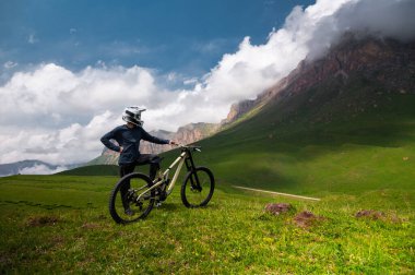 Kasklı ve koruyucu maskeli bir erkek bisikletçi. Dağlık arazide MTB sürücüsü destansı kayaların arka planına karşı