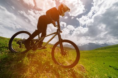 Kasklı ve koruyucu maskeli bir erkek bisikletçi. Dağlık arazide MTB sürücüsü destansı kayaların arka planına karşı