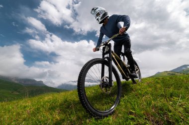 Dağ bisikletçisi çimenli bir yamaçtan aşağı iniyor. Enduro dağ bisikleti. Bir dağ manzarasına karşı MTB.