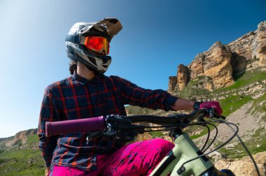 Güneşli bir günde dışarıda bisikletin üstünde duran bir bisikletçinin portresi. Erkek sporcu dinleniyor ve güzel dağ manzarasının tadını çıkarıyor. Kask ve eldiven takıyor. Etkin eğlence kavramı.