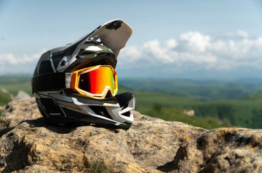 Tepe aşağı inen siyah beyaz bir bisiklet kaskının yan görüntüsü. Doğanın arka planına ve kümülüs bulutlu dağ manzarasına karşı ekstrem spor malzemeleri..