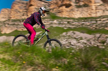 Profesyonel bisikletçi çimenler arasında kayalık bir yolda hızla ilerliyor. Dağlarda ekstrem spor.