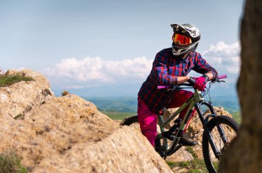 Bisikletli adam maske takıyor ve kaskını takmış tepelerde bisikletinin tepesinde dikiliyor. Dağ bisikleti için alan kopyası arka planı.