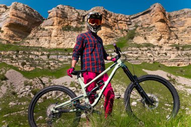 Kasklı ve koruyucu maskeli bir erkek bisikletçi. Dağlık arazide MTB sürücüsü destansı kayaların arka planına karşı
