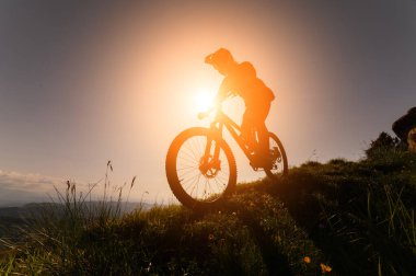 Dağ bisikletçisi çimenli bir yamaçtan aşağı iniyor. Enduro dağ bisikleti. Bir dağ manzarasına karşı MTB. Siluet