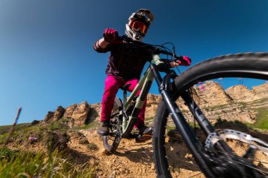 Kasklı ve koruyucu maskeli bir erkek bisikletçi. Dağlık arazide MTB sürücüsü destansı kayaların arka planına karşı