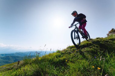 Dağ bisikletçisi çimenli bir yamaçtan aşağı iniyor. Enduro dağ bisikleti. Bir dağ manzarasına karşı MTB.