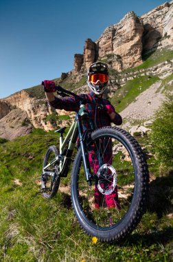 Bisiklet kasklı sporcu, destansı dağların ve manzaranın arka planına inmeden önce ayakta ve dinleniyor. MTB disiplin geçmişi. Dağ bisikleti için alan kopyalama arka planı.