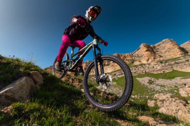Dağ bisikletçisi çimenli bir yamaçtan aşağı iniyor. Enduro dağ bisikleti. Bir dağ manzarasına karşı MTB.