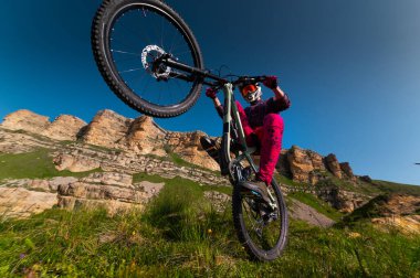 Genç adam arka tekerlekte dağ bisikletiyle havada süzülüyor. Fitness, ekstrem sporlar ve açık havada bisiklet, atlama ve macera için bir adamla dağ bisikleti. Adrenalin müptelası, performans ve sporcuyla birlikte açık havada eylem için gösteri yapıyor.