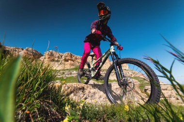 Kasklı ve koruyucu maskeli bir erkek bisikletçi. Dağlık arazide MTB sürücüsü destansı kayaların arka planına karşı