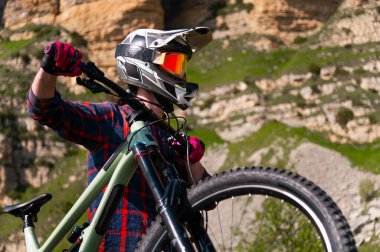 Kasklı ve koruyucu maskeli bir erkek bisikletçi. Dağlık arazide MTB sürücüsü destansı kayaların arka planına karşı