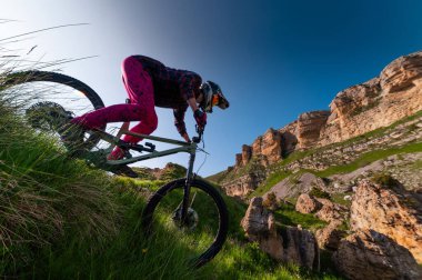 Dağ bisikletçisi çimenli bir yamaçtan aşağı iniyor. Enduro dağ bisikleti. Bir dağ manzarasına karşı MTB.