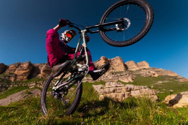 Dağ bisikletçisi Wheelie çalıyor. Bir dağ bisikletçisi kayalık dağların arka planında bir tekerlek çalar...