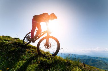 Dağ bisikletçisi çimenli bir yamaçtan aşağı iniyor. Enduro dağ bisikleti. Bir dağ manzarasına karşı MTB.