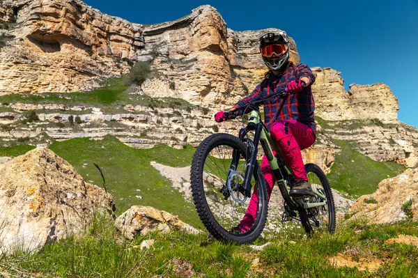 Koruyucu kasklı ve eldivenli, parlak elbiseli bir gencin portresi, yokuş aşağı bir bisiklette oturuyor ve uzaklığa bakıyor. Dağlarda aşırı dinlenme.