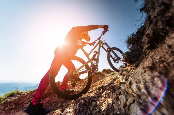 Dağ bisikletçisi kayalık yolda. Erkek bir bisikletçi bisikletini uçuruma itiyor, yürüyerek tırmanıyor. Ekstrem sporlar ve perde arkasındaki hayatları.