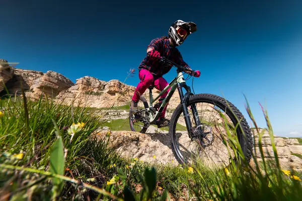Dağ bisikletçisi çimenli bir yamaçtan aşağı iniyor. Enduro dağ bisikleti. Bir dağ manzarasına karşı MTB.