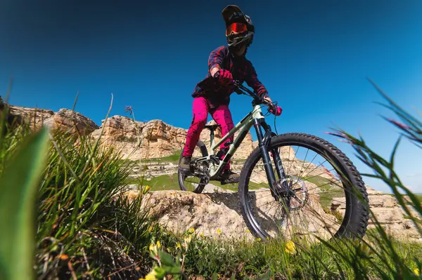 Kasklı ve koruyucu maskeli bir erkek bisikletçi. Dağlık arazide MTB sürücüsü destansı kayaların arka planına karşı