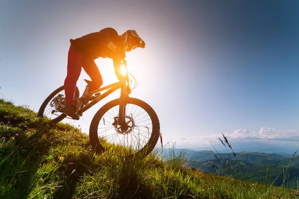 Kasklı ve koruyucu maskeli bir erkek bisikletçi. Dağlık arazide MTB sürücüsü destansı kayaların arka planına karşı