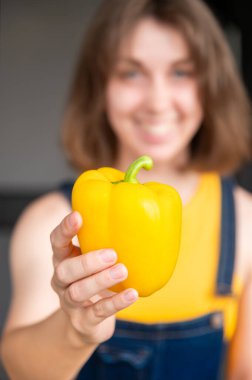 Mutfakta sarı dolmalık biber tutan genç beyaz kadın. Sağlıklı yaşam tarzı ev hanımlığı, vejetaryenlik, vejetaryenlik.