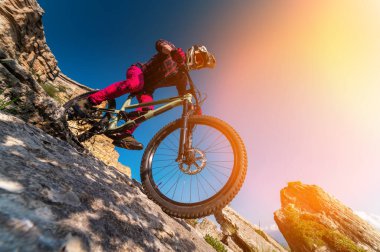 Kayalık dağ patikasındaki dağ bisikletçisi. Kayaya binen erkek bisikletçi. Kırmızı elbiseli bisikletçi kayalık yamaçtan aşağı iniyor. Ekstrem spor konsepti.