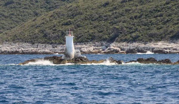 Kayalık sahilde küçük, beyaz bir deniz feneri. Dalgalar kıyıya vuruyor..