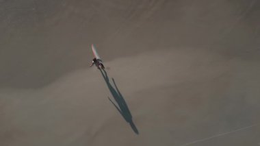 Kadın sörfçü havası. Sörf tahtası ile kumlu sahilde yürüyen kadın.