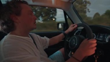 Uykulu genç adam esniyor ve arabayı alacakaranlıkta bir otoyolda sürüyor.