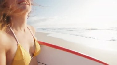 Seksi sörfçü. Bikinili genç mutlu kadın kumlu sahilde sörf tahtasıyla yürüyor.